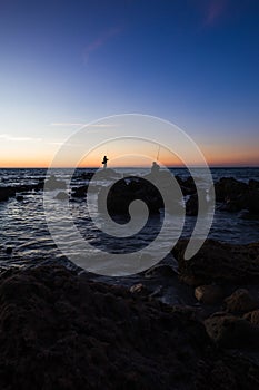 Fisherman fishing from rocks at sunset