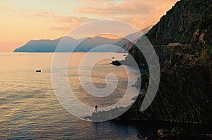 Fisherman with a fishing rod on the edge of the rock. Aerial nature landscape view of rocks descend into the Ligurian Sea