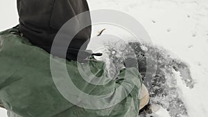 Fisherman with fishing rod is fishing in ice hole on frozen lake. Man is catching fish on ice frozen pond at winter fishing