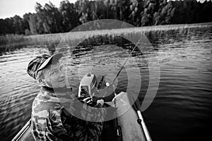 Fisherman fishing rod on the river on a rubber boat. Black and white photo.