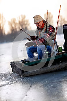 Fisherman with fishing rod sit on frozen river in the winter