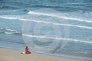 A fisherman with a fishing rod sitting on the seashore