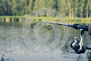 A fisherman with fishing rods, a spinning reel on the river bank. the lake has no focus. Sunrise. Fishing for pike, perch, carp.