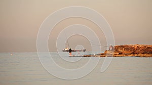 A fisherman is fishing in the sea at dawn, A fisherman on the rock against dawn sky, Silhouettes of fishermen with