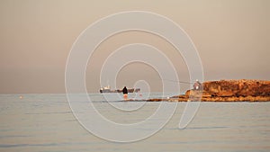 A fisherman is fishing in the sea at dawn, A fisherman on the rock against dawn sky, Silhouettes of fishermen with