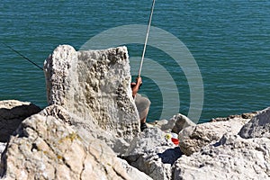 A fisherman is fishing with two fishing poles behind a rock Italy, Europe