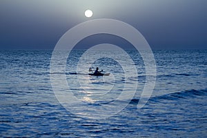 Fisherman fishing in the wavy  ocean at night under the gleaming full moon