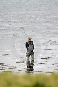 A fisherman fishing wearing waders and holding a fishing rod photo