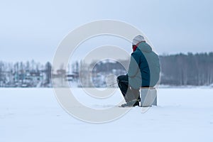 Fisherman on a frozen snowy lake. Back view. Grey sky. Forest in the snow on the horizon.