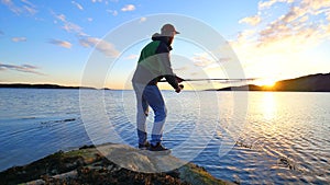 The fisherman with green sporty backpack is checking fishing equipment. Man prepare pushing bait on fishing line and throw lure