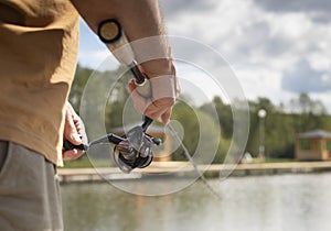 Fisherman hands holding reel rod, spoon-bait and fishing over lake, close up