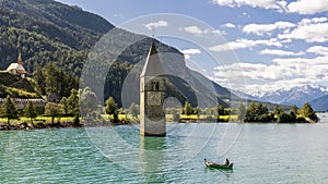 Fisherman in his boat near the submerged bell tower in Resia lake, Curon, South Tyrol, Italy