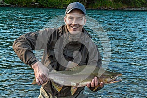 A fisherman holding up a large pink `humpback` salmon at sunset