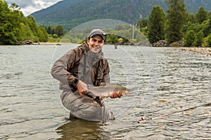 A fisherman holding up a male humpback pink salmon while wading in a river