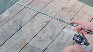 Fisherman holds a fishing rod in his hands and turns the reel standing on a wooden pier. Spinning fishing on the river