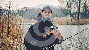 Fisherman holds a perch in his hand