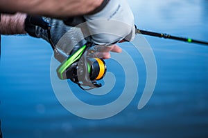 The fisherman holds a spinning rod in his hands. Angler with spinning rod and fishing reel. Hands and spinning on the background