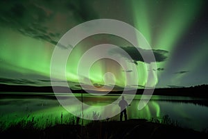 fisherman at lake under a night sky aglow with aurora from a geomagnetic storm