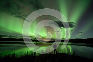 fisherman at lake under a night sky aglow with aurora from a geomagnetic storm photo