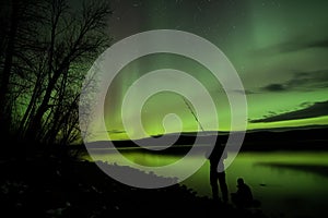 fisherman at lake under a night sky aglow with aurora from a geomagnetic storm photo