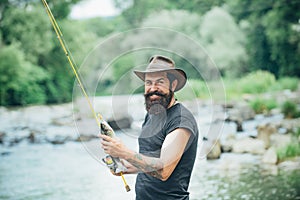 Fisherman man on river or lake with fishing rod. Hipster bearded man catching trout fish.