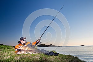 Fisherman man sits on the shore. In the hands of a fishing rod s