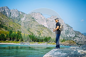 Fisherman on the mountain river at the nice summer day. Trout fly fishing in the mountain river with mountains in background