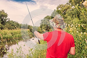 Fisherman in a panama hat and a red t-shirt casts a spinning rod