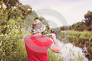 Fisherman in a panama hat and a red t-shirt casts a spinning rod