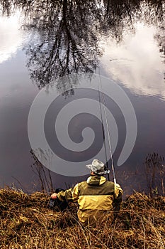 A fisherman on a picturesque lake is resting with a fishing rod in his hands. Catching freshwater fish. Vertical photo