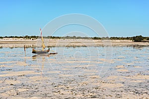 Fisherman piroga small fishing boat with sail waiting at the low tide coast on sunny day