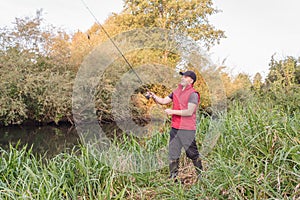 Fisherman in a red vest with a fishing rod on the shore