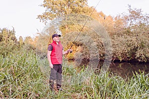 Fisherman in a red vest with a fishing rod on the shore