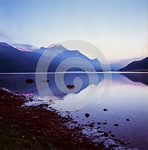 A fisherman rowing among the fog on the lake of Silvaplana in the Engadin valley at sunrise with mountains reflecting in the water