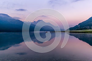 A fisherman rowing among the fog on the lake of Silvaplana in the Engadin valley at sunrise with mountains reflecting in the water