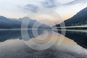 A fisherman rowing among the fog on the lake of Silvaplana in the Engadin valley at sunrise with mountains reflecting in the water