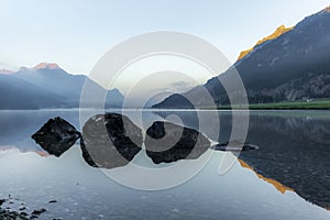 A fisherman rowing among the fog on the lake of Silvaplana in the Engadin valley at sunrise with mountains reflecting in the water