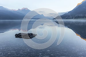 A fisherman rowing among the fog on the lake of Silvaplana in the Engadin valley at sunrise with mountains reflecting in the water