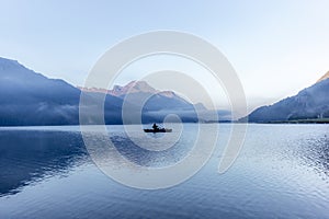 A fisherman rowing among the fog on the lake of Silvaplana in the Engadin valley at sunrise with mountains reflecting in the water