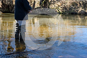 Fisherman with rubber boots trout fishing in a creek on a sunny day. Angler casting artificial bait in a river