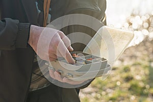 The fisherman's hands are holding a plastic box with a variety of lures and fishing hooks