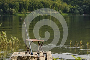 Fisherman`s place. A chair, a fishing rod and fish bait rests on a stone against the backdrop of a large river