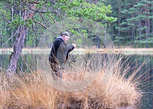fisherman on the shore of a swamp lake, forest and swamp vegetation, rainy and cloudy day