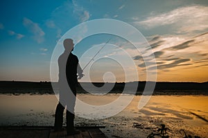 A fisherman silhouette fishing at sunset. Freshwater fishing, catch of fish.