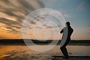 A fisherman silhouette fishing at sunset. Freshwater fishing, catch of fish.