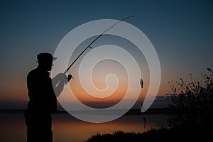 A fisherman silhouette fishing at sunset. Freshwater fishing, catch of fish