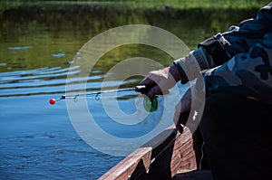 Fisherman sits in a boat with a small winter fishing rod on the river