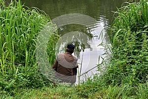 The fisherman sits in the reeds and catches fish.