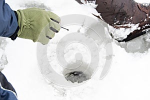 Fisherman sitting on frozen water near drilled hole in ice. Winter fishing concept