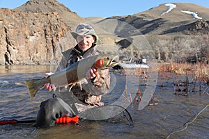 Fisherman sitting in river holding a steelhead trout